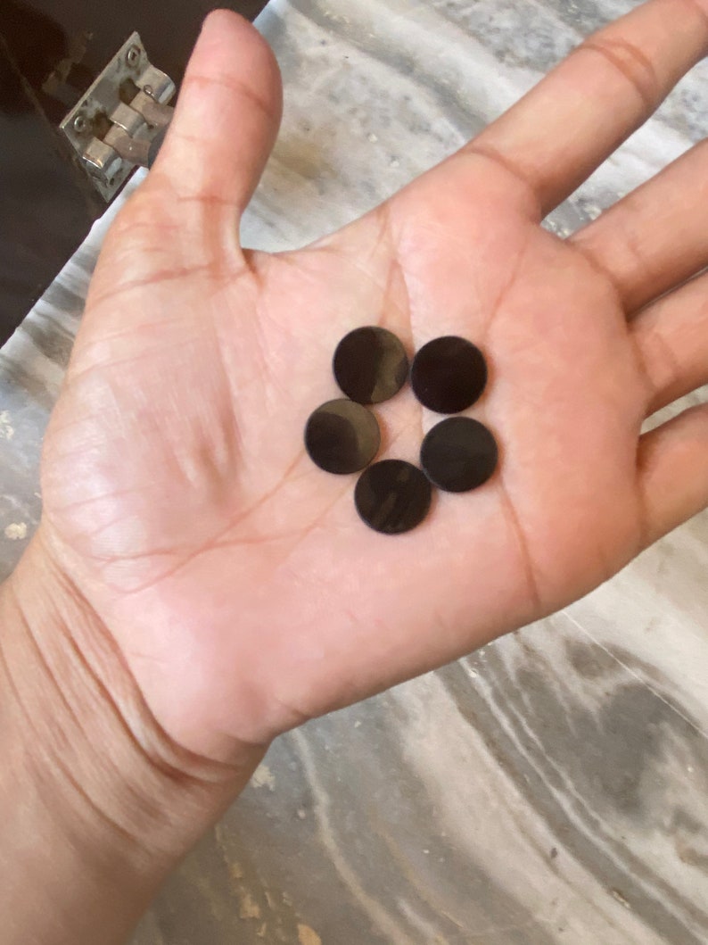 May include: Five black round buttons, possibly for a craft project or clothing, are displayed on the palm of a hand.