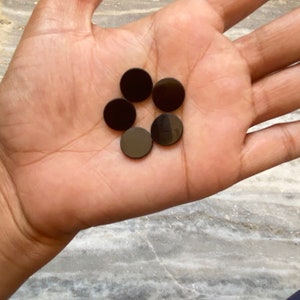 May include: Six black round buttons, arranged in a circle, in the palm of a hand.