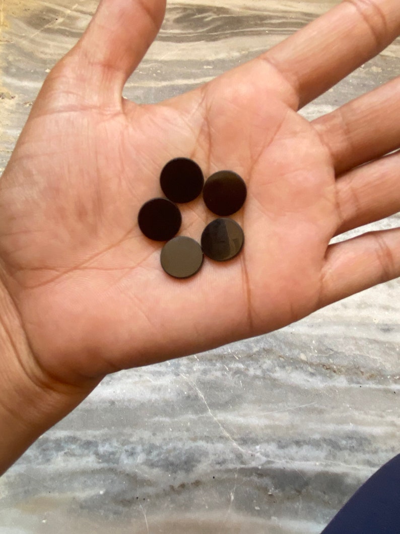 May include: Six black round buttons, arranged in a circle, in the palm of a hand.