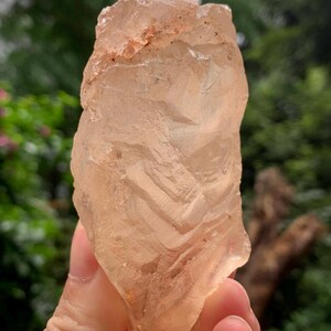 Puede incluir: Un espécimen de cristal crudo y translúcido de color melocotón con una forma irregular y dentada. La superficie presenta facetas naturales, crestas y sutiles inclusiones internas, mostrando un tono naranja pálido en toda la pieza.