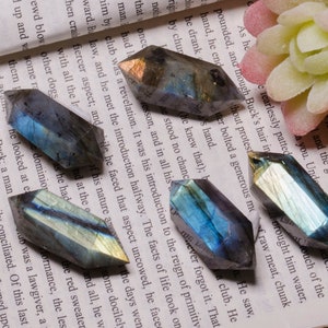 May include: A collection of six iridescent labradorite crystal points, each with a unique blue and green color pattern. The crystals are arranged on a page of a book with text.
