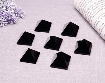 May include: Seven black obsidian pyramids of various sizes arranged on a grey fabric surface. The pyramids are smooth and polished.