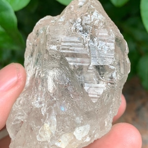 May include: A large, clear quartz crystal with a rough, natural surface. The crystal has a milky white colour and shows iridescent rainbow colours.