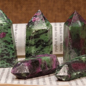 Peut inclure: Cinq pointes de pierres précieuses vertes, noires et roses, également connues sous le nom de rubis en zoïsite, disposées sur une page de livre.