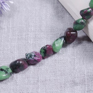 May include: A strand of green and pink gemstone beads. The beads are irregularly shaped and have a natural, polished finish.