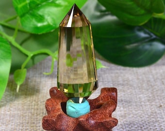May include: A clear, faceted citrine crystal point with a golden hue, resting on a wooden stand with a turquoise base. The crystal is approximately 2 inches in length.
