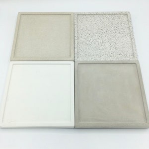 May include: Four square concrete trays in different colours and finishes. The trays are white, light grey, beige, and speckled grey.
