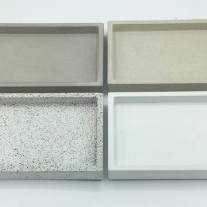 May include: Four rectangular trays made of concrete. The trays are in different colours and textures. Two trays are a light beige colour, one tray is a speckled white and grey, and one tray is a solid white.