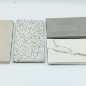 May include: Four rectangular stone tiles in varying colours and textures. The tiles include a light beige, speckled white and grey, solid grey, and white with grey veining. The tiles are arranged on a white surface.