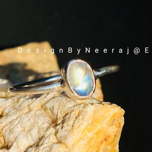 May include: A silver ring with a light blue oval gemstone. The ring is set on a textured rock.