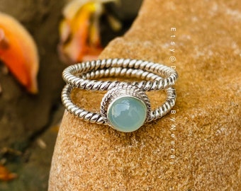 May include: A silver ring with a twisted band and a light blue gemstone. The ring is set on a brown rock.
