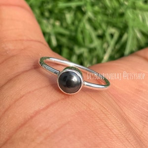 Puede incluir: Un anillo de plata con una piedra preciosa negra. El anillo est&aacute; en el dedo de una persona.