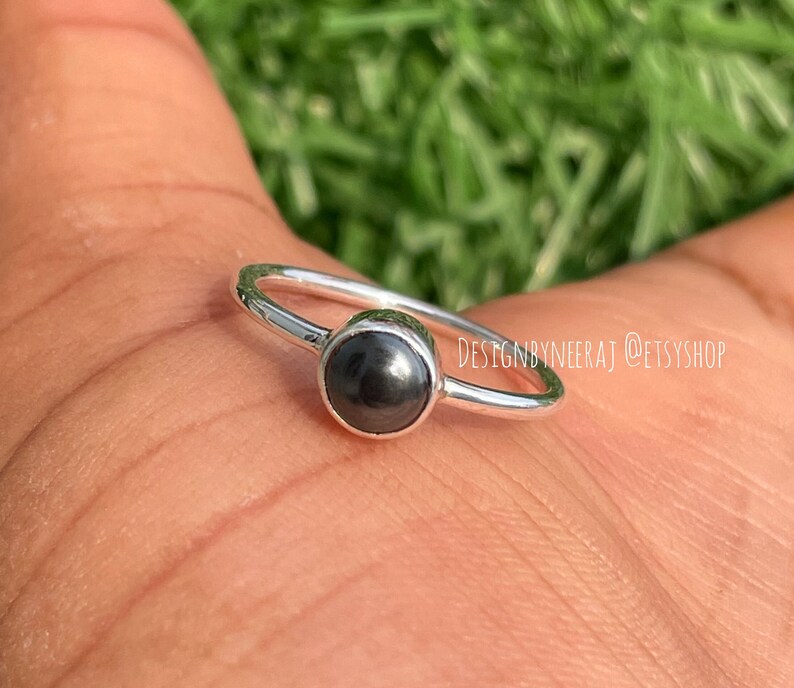 Puede incluir: Un anillo de plata con una piedra preciosa negra. El anillo est&aacute; en el dedo de una persona.