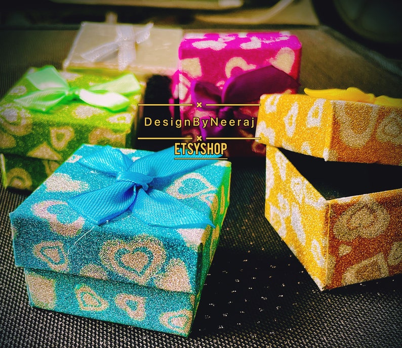 Puede incluir: Cuatro peque&ntilde;as cajas de regalo con purpurina y dise&ntilde;os estampados. Las cajas son de varios colores, incluyendo verde, azul, rosa y amarillo. Las cajas tienen lazos y est&aacute;n dispuestas sobre una superficie negra. El texto "DesignByNeeraj ETSYSHOP" es visible en la imagen.