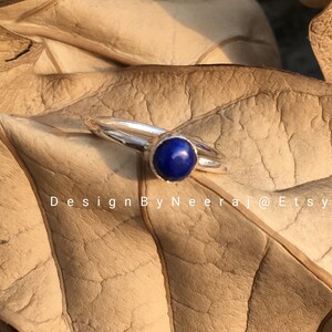 May include: A silver ring with a dark blue gemstone. The ring is on a brown leaf.