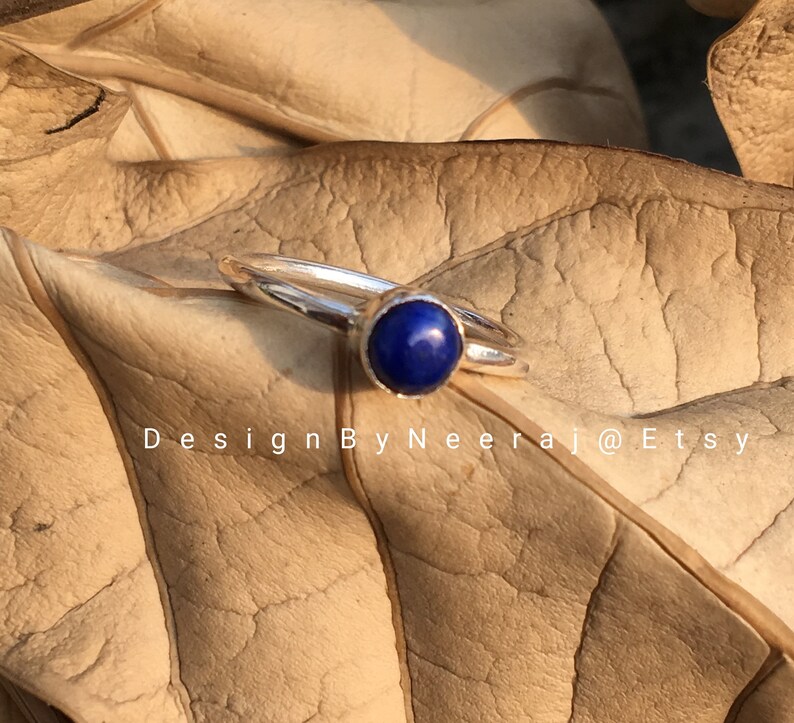 May include: A silver ring with a dark blue gemstone. The ring is on a brown leaf.