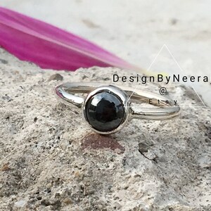 Puede incluir: Un anillo de plata con una piedra preciosa negra. El anillo est&aacute; sobre una superficie texturizada. DesignByNeeraj @ Etsy