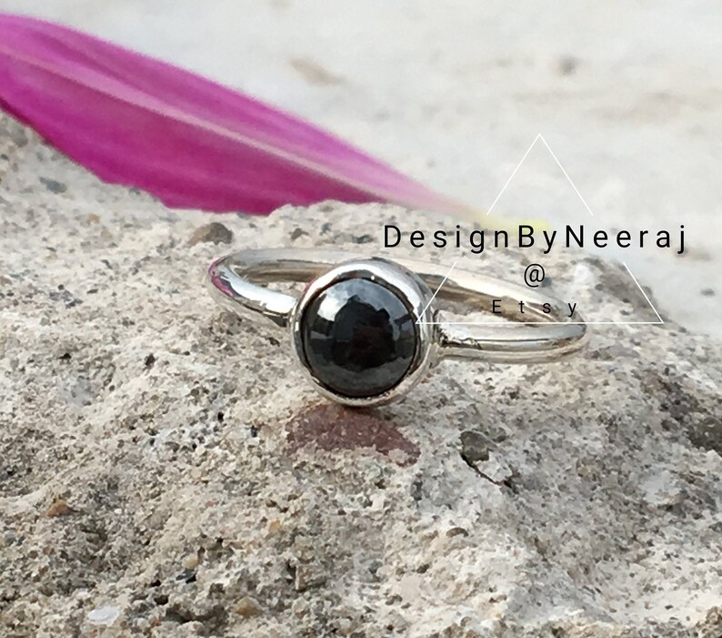 Puede incluir: Un anillo de plata con una piedra preciosa negra. El anillo est&aacute; sobre una superficie texturizada. DesignByNeeraj @ Etsy