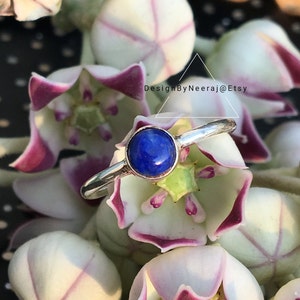 May include: A silver ring with a blue lapis lazuli gemstone. The ring is set against a background of white and purple flowers.