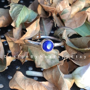 May include: A silver ring with a round blue lapis lazuli gemstone. The ring is set against a background of brown leaves.
