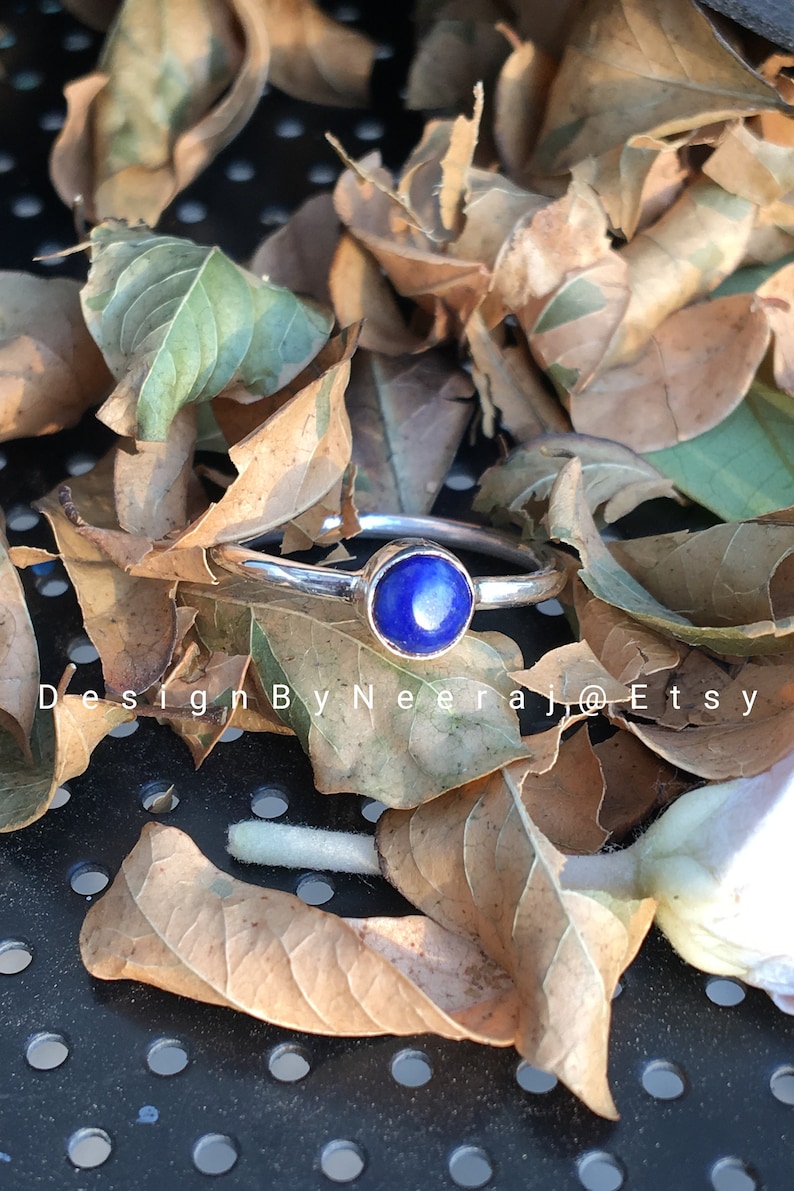 May include: A silver ring with a round blue lapis lazuli gemstone. The ring is set against a background of brown leaves.