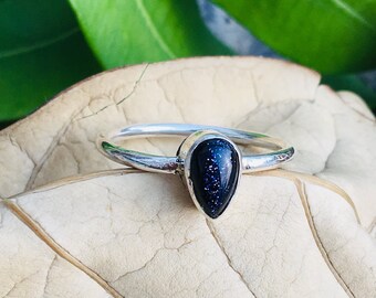 May include: A silver ring with a teardrop-shaped blue gemstone. The gemstone has a sparkly, speckled texture.