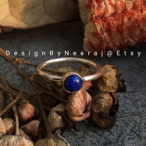 May include: A silver ring with a blue lapis lazuli gemstone. The ring is set on a background of dried flowers.