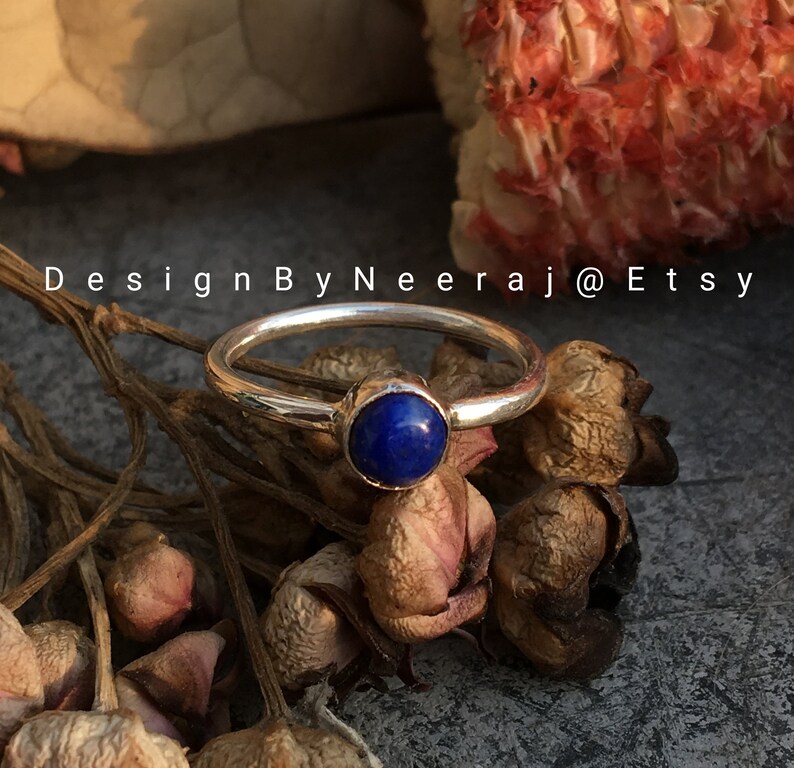 May include: A silver ring with a blue lapis lazuli gemstone. The ring is set on a background of dried flowers.