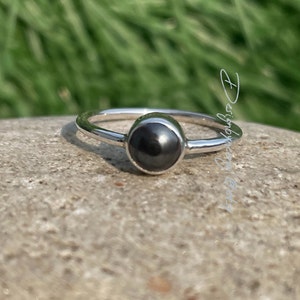 Puede incluir: Un anillo de plata con una piedra preciosa negra. El anillo es simple y elegante.