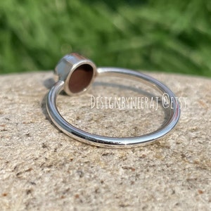 Puede incluir: Un anillo de plata con una piedra ovalada de color rojo oscuro. El anillo est&aacute; sobre una roca gris.