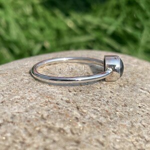 Puede incluir: Un anillo de plata con una piedra preciosa negra. El anillo es simple y elegante.