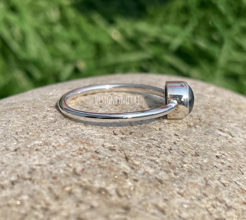 Puede incluir: Un anillo de plata con una piedra preciosa negra. El anillo es simple y elegante.