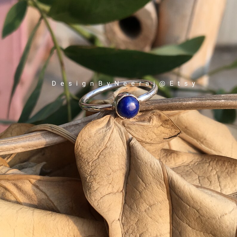 May include: A silver ring with a blue gemstone. The ring is set on a brown background.