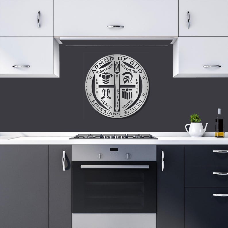 May include: A silver metal wall art piece with the text "Armor of God" and other religious symbols. The circular design includes the words "Righteousness", "Salvation", "Faith", "Peace", "Truth", and "Ephesians 6:10-20". The art is displayed in a kitchen setting.