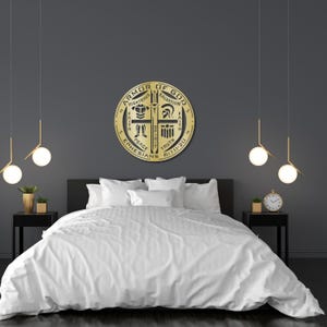 May include: A gold-colored, circular wall hanging with the text "Armor of God" and other religious symbols. The artwork is mounted above a bed with white bedding. The room has dark gray walls and modern lighting fixtures.