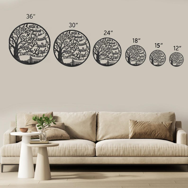 May include: Black metal wall art featuring a tree design within a circle, with the text "Everything that has breath praise the Lord." Available in sizes from 12" to 36" diameter. The art is displayed above a beige sofa.