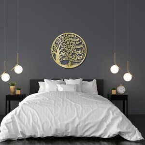 May include: A gold-colored metal wall art piece in a circular shape, featuring a tree design with the words "Let everything that has breath praise the Lord". The art is mounted above a bed with white bedding.