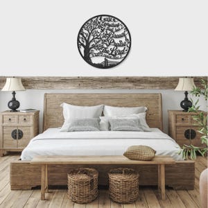 May include: A black metal wall art piece in a circular shape, featuring a tree design with the words "Let everything that has breath praise the Lord" and Psalm 150:6. The art is mounted above a wooden bed frame.