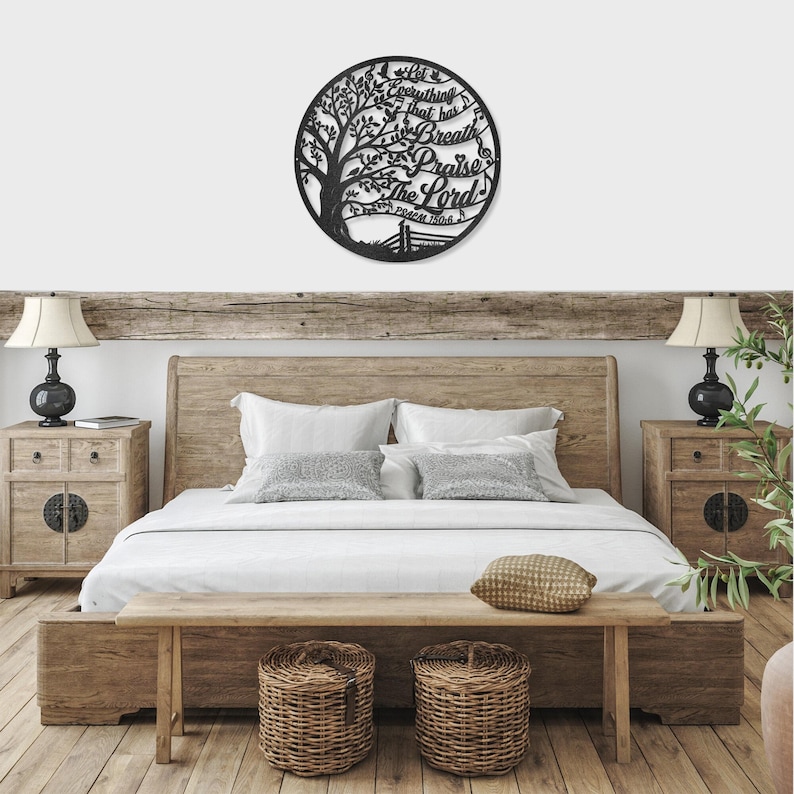 May include: A black metal wall art piece in a circular shape, featuring a tree design with the words "Let everything that has breath praise the Lord" and Psalm 150:6. The art is mounted above a wooden bed frame.