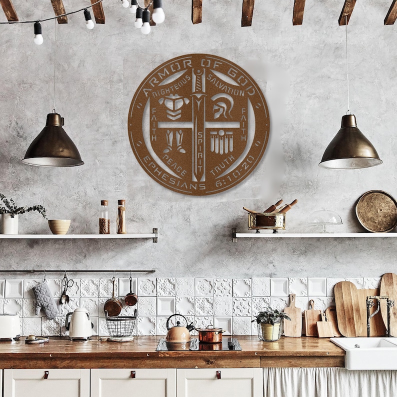 May include: A circular, bronze-colored metal wall art piece with the words "Armor of God" and other religious text. The design includes a sword, helmet, and other symbols. The artwork is mounted on a gray wall in a kitchen setting.