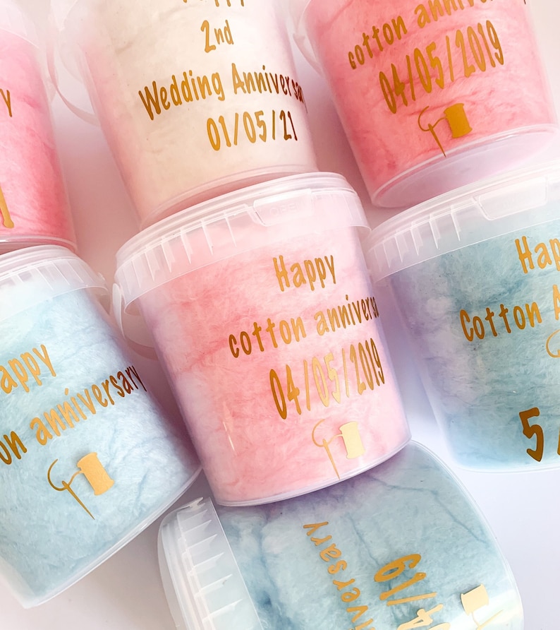 Pu&ograve; includere: Una collezione di sei contenitori di plastica trasparente riempiti di zucchero filato rosa, blu e bianco. Ogni contenitore ha un'etichetta dorata con una data e un messaggio diversi, come "Happy cotton anniversary 04/05/2019" e "2nd Wedding Anniversary 01/05/21".