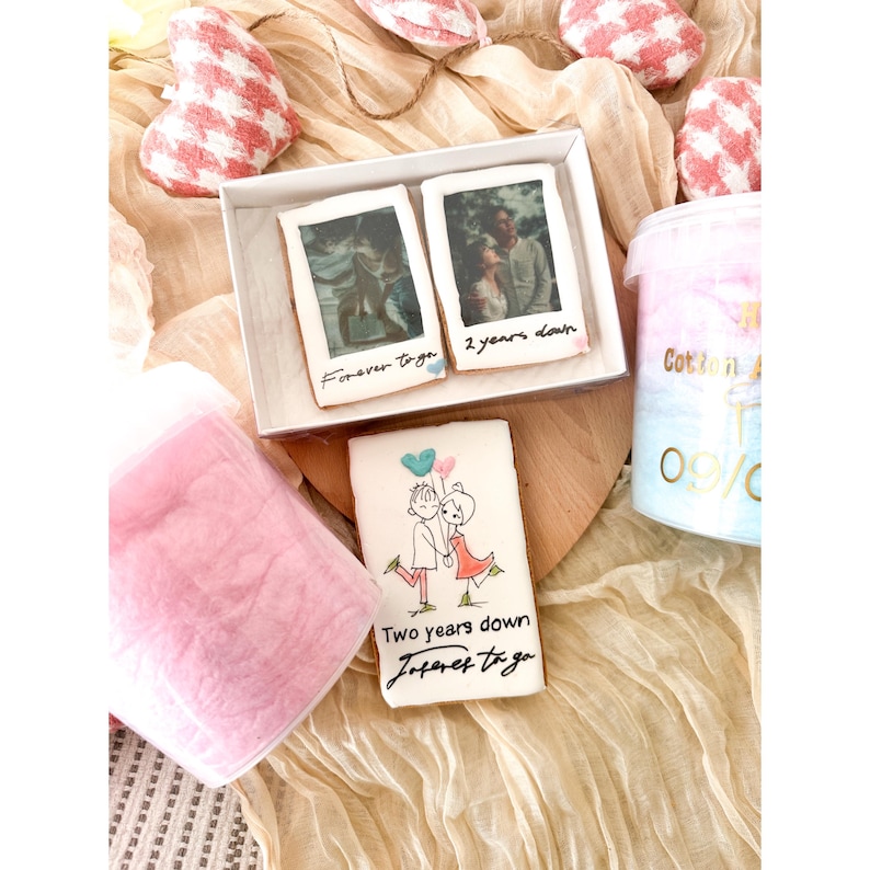Pu&ograve; includere: Un set regalo per una coppia che celebra il suo anniversario. Il set include due biscotti decorati, uno con una foto della coppia e il testo "Forever together" e l'altro con una foto della coppia e il testo "Two years down". Il set include anche un contenitore di zucchero filato rosa.
