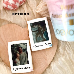 Pu&ograve; includere: Due biscotti decorati con foto e messaggi scritti a mano. Il biscotto in alto ha una foto di una coppia e il testo "forever together". Il biscotto in basso ha una foto di una coppia e il testo "2 years down".