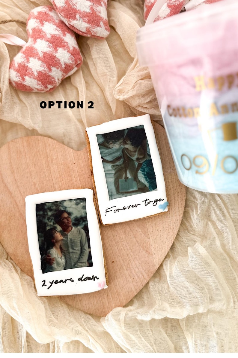 Pu&ograve; includere: Due biscotti decorati con foto e messaggi scritti a mano. Il biscotto in alto ha una foto di una coppia e il testo "forever together". Il biscotto in basso ha una foto di una coppia e il testo "2 years down".