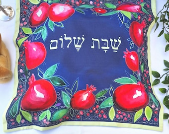 Könnte beinhalten: Ein blauer Stoff-Challah-Überzug mit gelbem Rand. Der Überzug ist mit Granatäpfeln und grünen Blättern verziert. Der hebräische Text "Shabbat Shalom" ist in Weiß auf dem Überzug geschrieben.