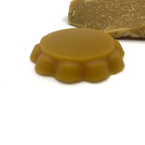 Puede incluir: Un bloque de cera de abeja redondo, de color amarillo dorado, con un borde festoneado.