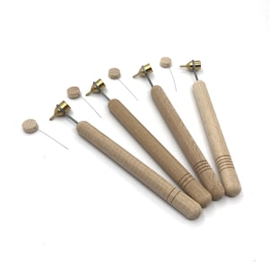 May include: Five wooden calligraphy pens with brass nibs and wooden caps. The pens are arranged in a fan shape on a white surface.
