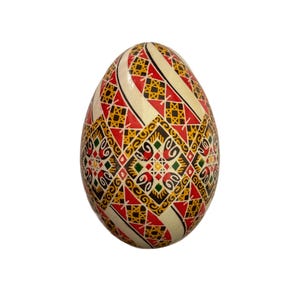 May include: A white egg decorated with a geometric pattern in red, yellow, black, and green. The pattern is intricate and includes squares, diamonds, and swirls.