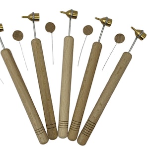 May include: A collection of wood-handled tools with brass tips, likely for crafts or art. Each tool has a wooden handle, a metal tip, and a small, round wooden piece attached. The tools are arranged in a fan shape.