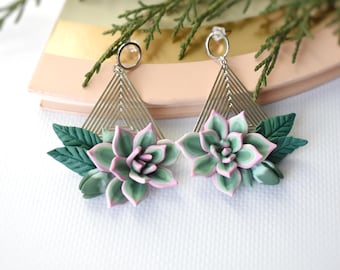 Puede incluir: Un par de pendientes geométricos plateados con detalles de flores de suculentas rosas y verdes.